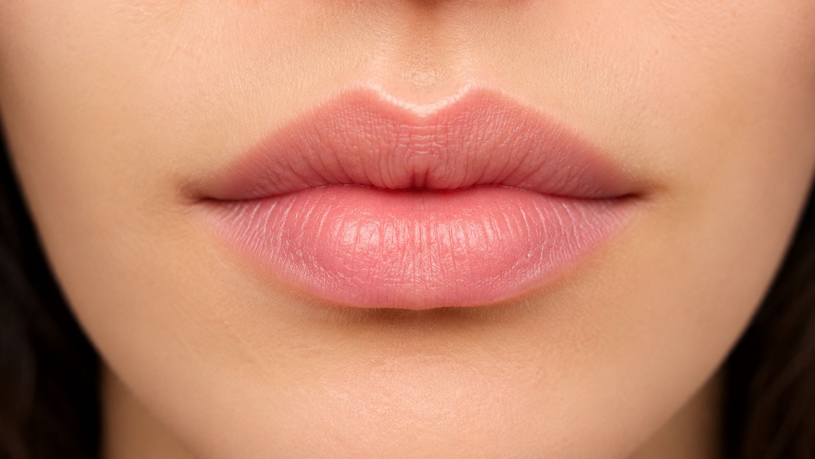 A close-up view of natural, well-defined human lips, highlighting a soft pink color and smooth skin texture.