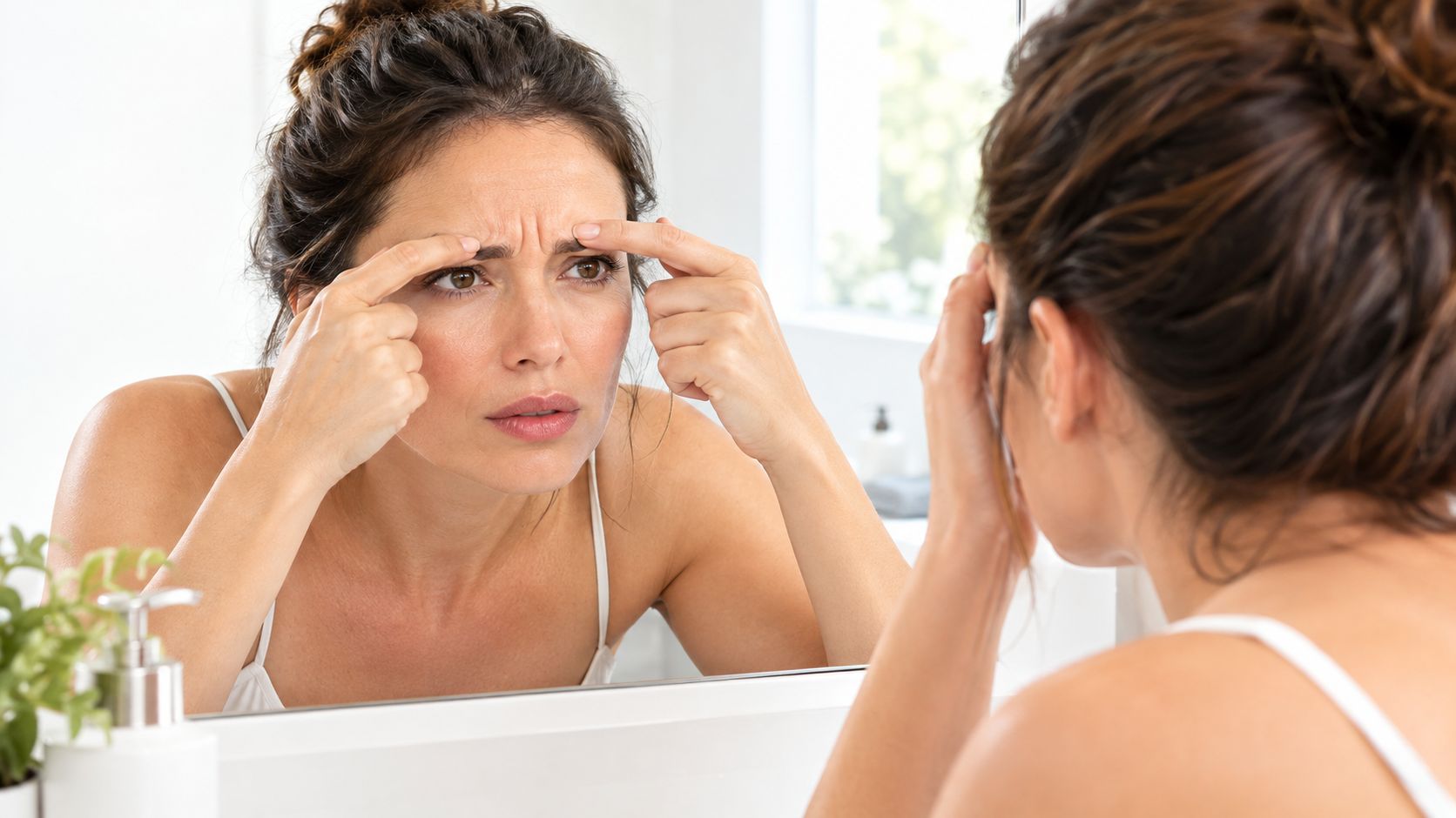A woman examining wrinkles between her eyebrows in the mirror before considering botox treatment.