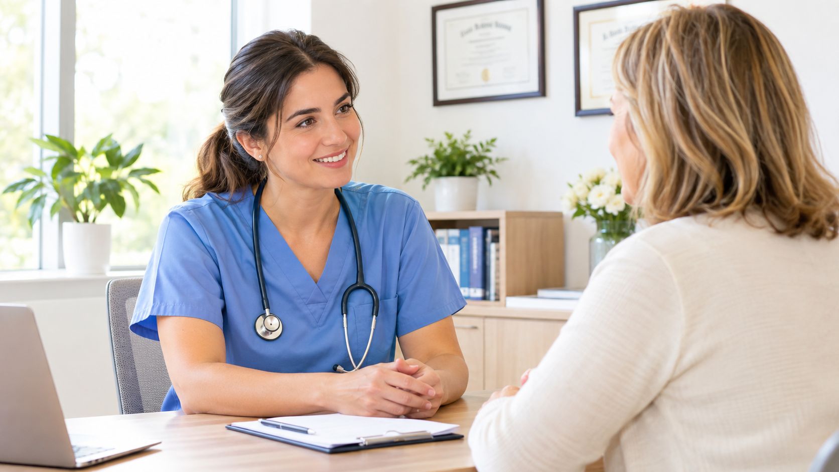A friendly female nurse in blue scrubs consulting with a patient in a bright medical office.